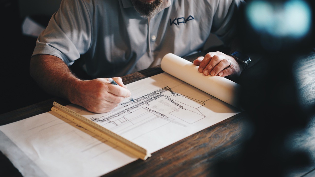 Architect drawing blueprints by hand at a wooden desk