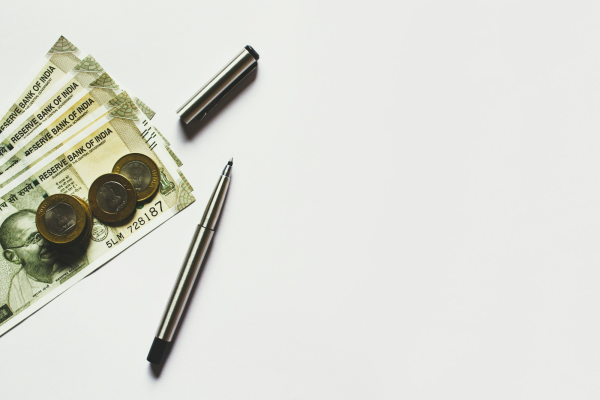 Indian rupee notes and coins with a pen on a white surface