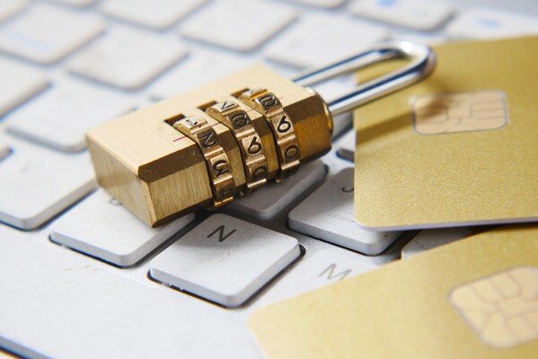 A combination padlock resting on a laptop keyboard beside gold credit cards