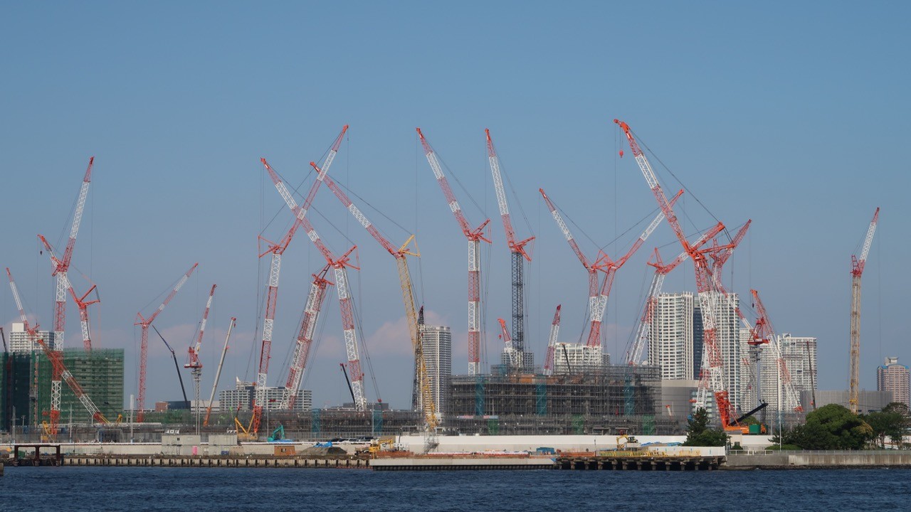 Many red-and-white cranes at a large construction site by the water - large-scale parallel work
