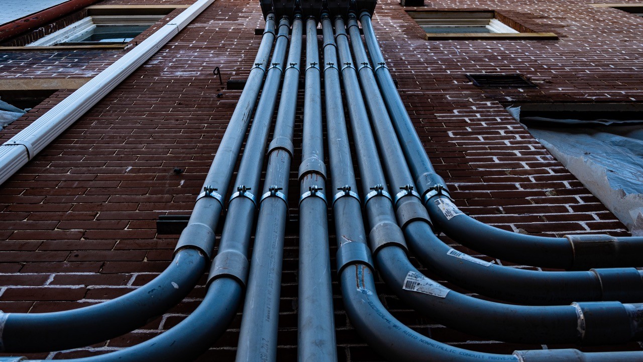 Pipes and conduits converging on a brick building facade - parallel pipelines merging