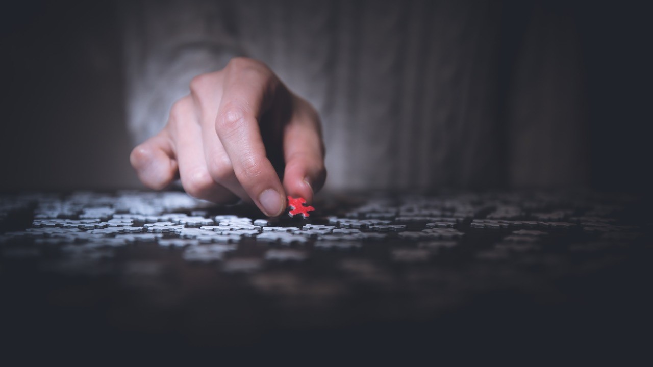 A hand picking up a single red puzzle piece from many grey pieces - finding the right module
