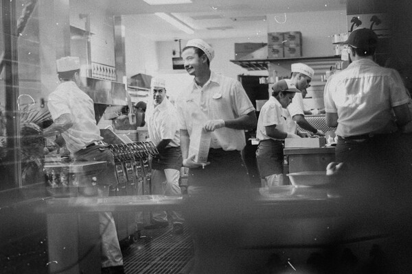 Black-and-white photo of fast-food kitchen staff working together at multiple stations