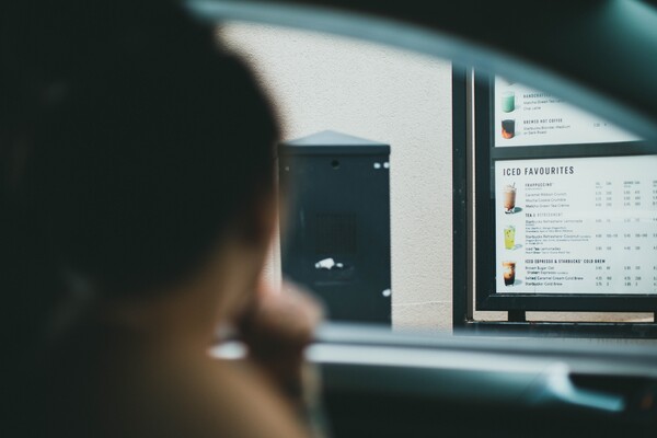 Person ordering at a drive-through window looking at a lit menu board from inside their car